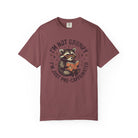 A maroon unisex t-shirt featuring a graphic of a raccoon wearing glasses and reading a book.