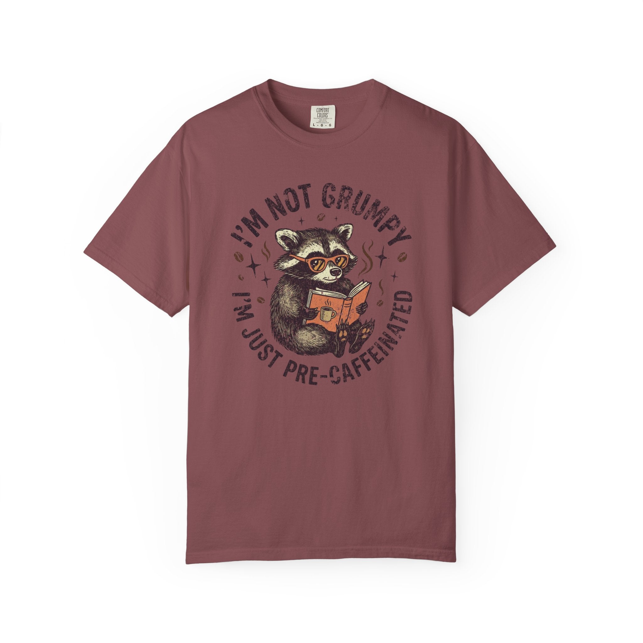 A maroon unisex t-shirt featuring a graphic of a raccoon wearing glasses and reading a book.