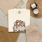 An ivory Comfort Colors t-shirt with a retro distressed coffee-themed graphic on a flat lay.