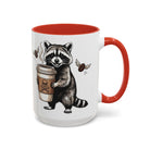 White ceramic mug with a red handle and interior, featuring a raccoon holding a coffee cup.