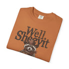 Orange t-shirt featuring a distressed graphic of a raccoon in a cowboy hat holding a coffee mug.