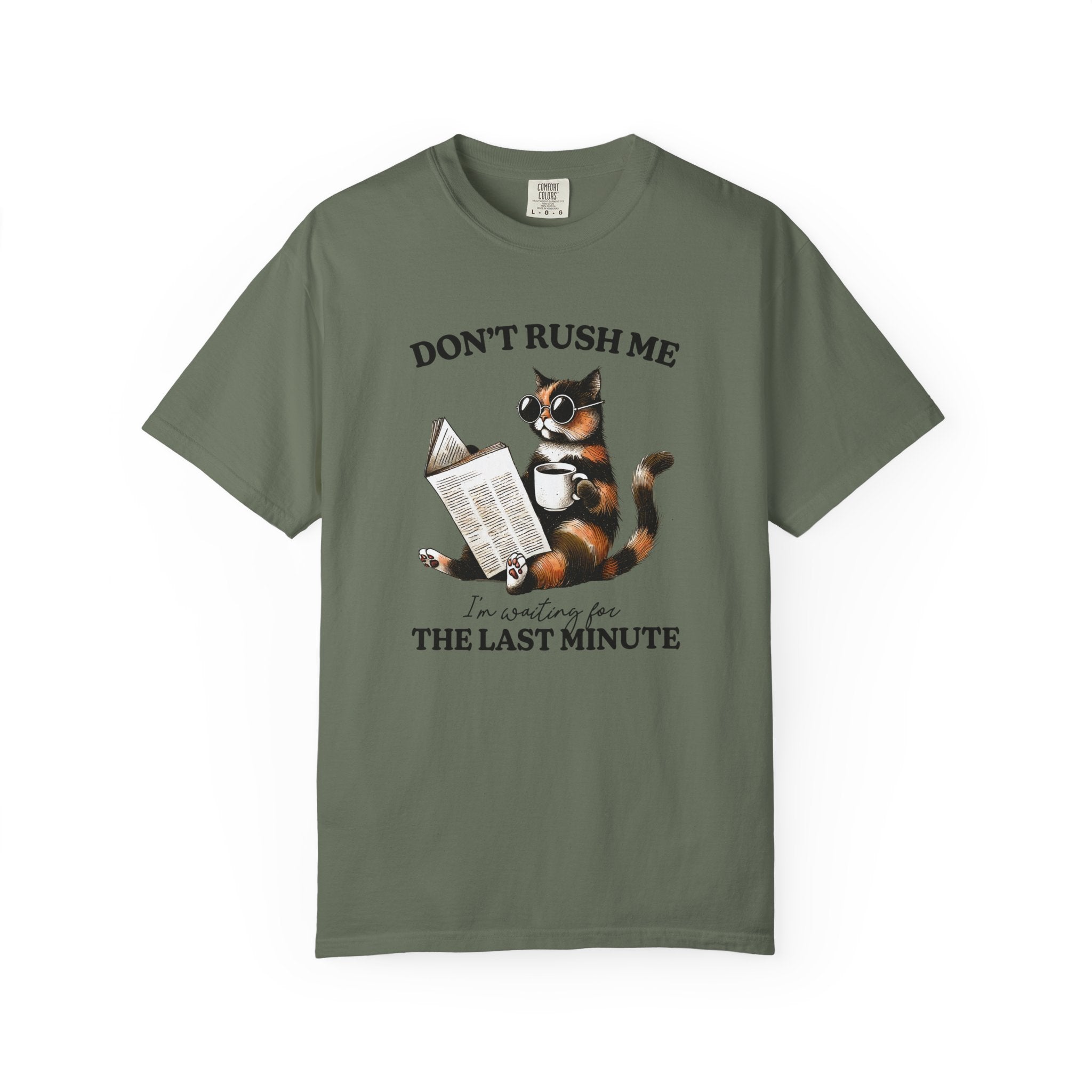 An olive green cotton t-shirt featuring a graphic of a cat wearing sunglasses, reading a book, and holding a coffee mug with the text Don't rush me, I'm waiting for the last minute.