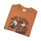 Folded orange t-shirt featuring a graphic of a rooster in a cowboy hat pouring coffee.