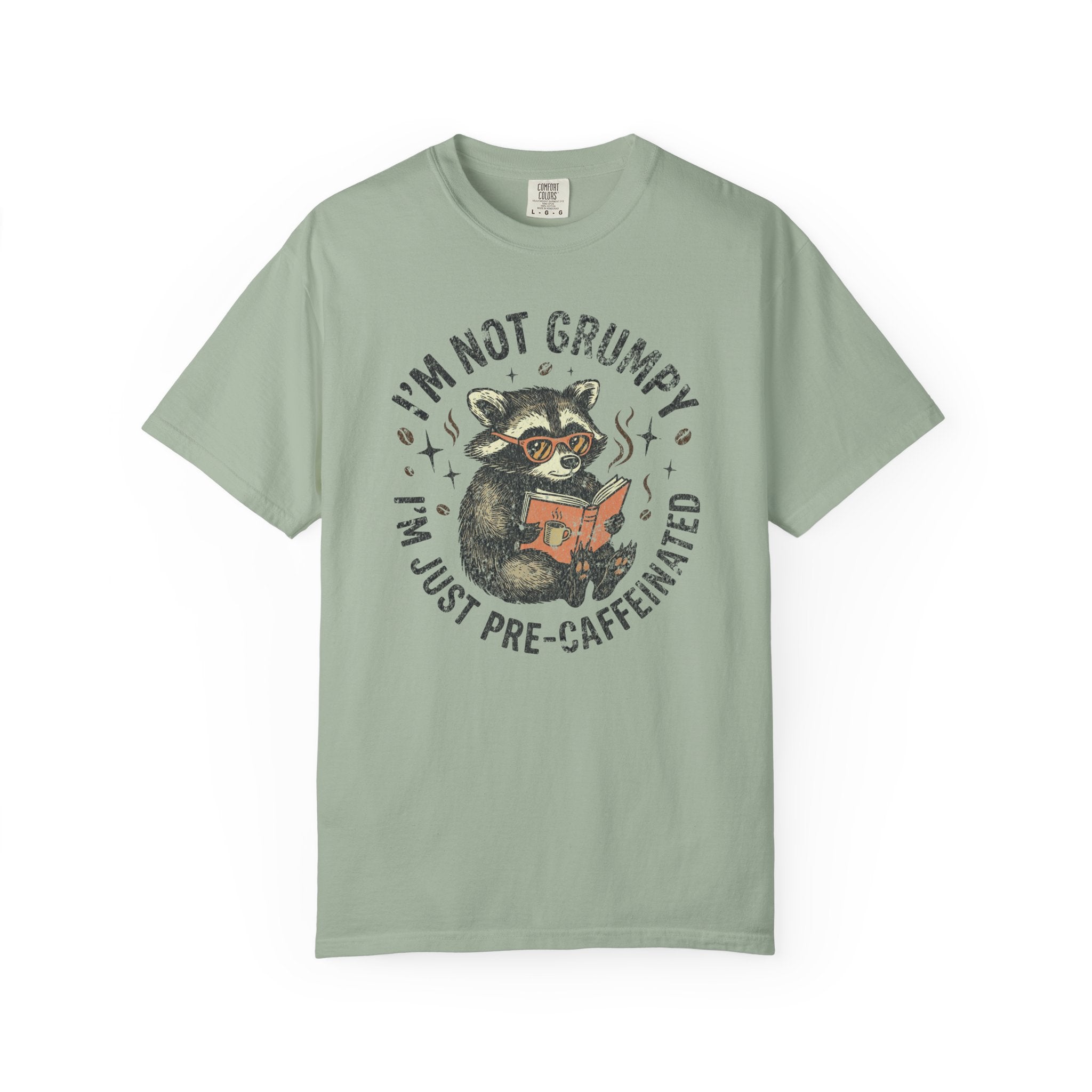 Sage green unisex t-shirt with a graphic of a raccoon wearing glasses and reading a book.