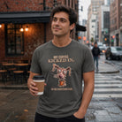 A man standing on a city street holding a takeaway coffee cup, wearing a dark gray graphic T-shirt with the text 'MY COFFEE KICKED IN. SO DID EVERYTHING ELSE.